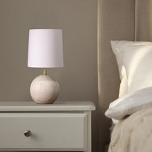 Mini table lamp with light fabric shade and textured ball base beside a bed