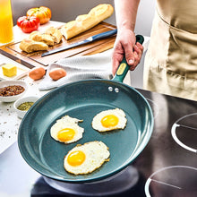 Nonstick frying pan holding three sunny-side-up eggs with dark green handle