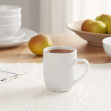 Glazed white stoneware mug with handle, filled with light brown beverage