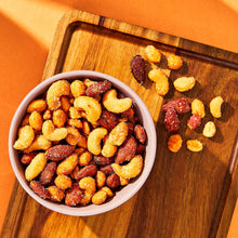 Hot honey coated cashews and almonds in bowl with nuts scattered on board