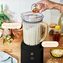 Blender pitcher with glass insert and gold handle on black base, being filled by hand