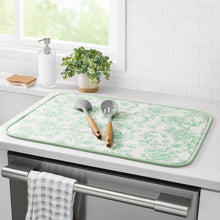 Green floral dish drying mat on kitchen counter with two utensils on top