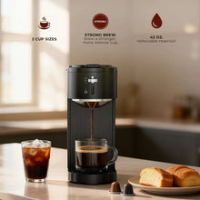 Black drip coffee maker brewing into glass cup with coffee grounds