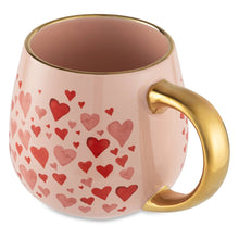 Pink ceramic mug with red hearts, gold-tone handle, and dark interior.