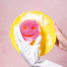 Scrub Mommy sponge being used: white side with pink scrub face, smiling design