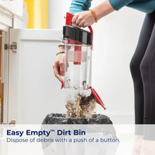 Person holding red upright vacuum dirt bin with clear container and red handle.