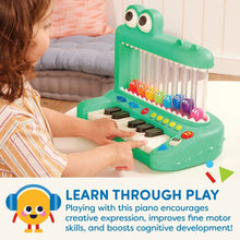 Green crocodile piano toy on table; child hand presses white and black keys