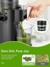 Black cold press juicer with hand adjusting a top dial and green juice in cup.