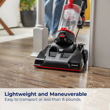 Upright vacuum on wood floor with clear dirt bin and floor brush head.