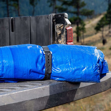 Black rubber strap securing a rolled bundle on a platform, holes on strap.