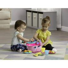 Kids playing with a pink picnic basket toy on a floor with colorful shape pieces