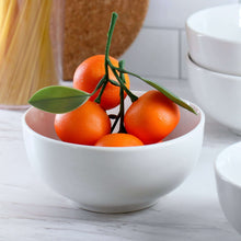 White porcelain bowl holding fresh oranges with green stems