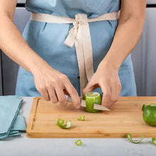 Stainless steel knife slicing a green pepper on a wooden cutting board
