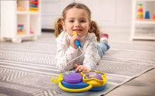 Child holding a toy microphone near a purple speaker boombox on floor.