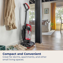 Compact upright vacuum with raised handle, red accents, and clear dirt bin.