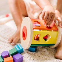 Toddler hands turning a wooden shape sorter drum with matching blocks