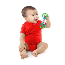Baby holding a green and clear shaker rattle toy with ball-shaped grips