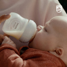 Philips Avent Natural baby bottle with pink accents, held to feed a baby