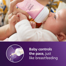 Pink Philips Avent Natural baby bottle tilted as baby drinks, white nipple
