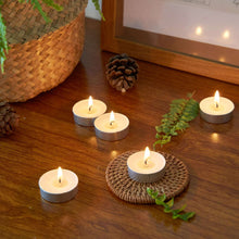 Lit white unscented tealight candles in metal cups on a wooden surface