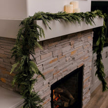 Green evergreen cedar garland looping along the edge of a fireplace mantel