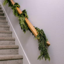 Green evergreen cedar garland with full branches hanging from a wood rail
