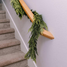 Green evergreen cedar garland draped over a light wood mounting rail