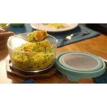Glass food storage container with teal snap lid holding a portion of food