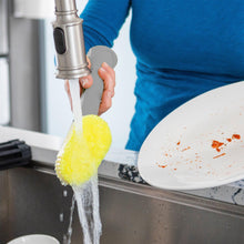 Dish wand spraying water with yellow sponge head over sink area