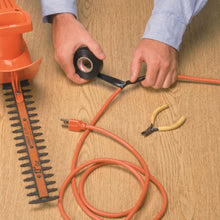 Black electrical tape being wrapped around orange electrical wires on wood