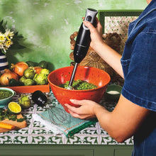 Immersion blender being used to blend in a red mixing bowl