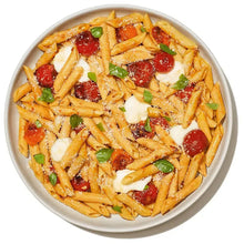 Bowl of penne pasta with tomato, melted cheese, and chopped herbs
