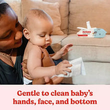 Baby holding a white baby wipe with wipes pack nearby