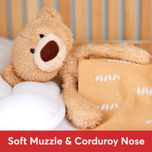 Beige teddy bear plush with dark oval nose patch and floppy limbs, lying down