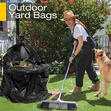 Black outdoor trash bag bundle with gathered top, near a yard cleanup scene