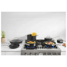 Hard anodized cookware set on gas range with black pans and covered pots