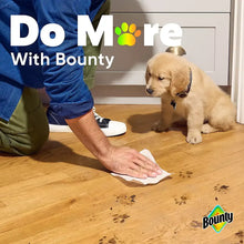 Paper towel sheet in use, held to wipe a wooden floor near a seated dog