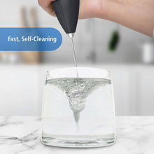 Handheld milk frother wand whisk submerged in a clear glass during cleaning