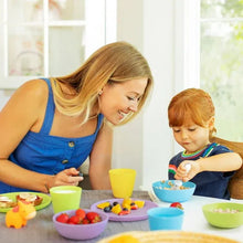 Toddler dining set in use: colorful bowls, cups, and utensils on tabletop.