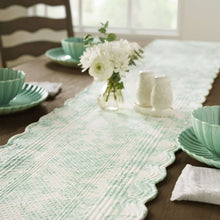 Quilted green-and-white fabric table runner with scalloped edges and wave-stitched quilting