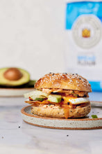 Topped sandwich on a plate with a blurred unbleached bread flour bag in back.