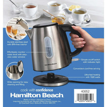 Stainless steel electric kettle on base with black handle, shown with a hand