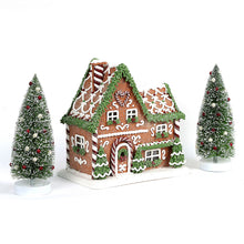 Prelit gingerbread house decoration with snowy pine trees, detailed roof and doors