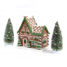 Prelit gingerbread house scene with two snowy pine trees and arched doorway