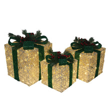 Three gold lighted gift boxes with green bows and pine branches, each with red berries