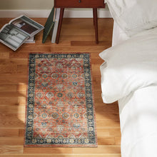 Red and multicolor ornate accent mat on hardwood floor beside a bed