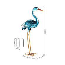 Heron statue pair—teal metal bird sculpture with orange beak and gold wire legs, round base.