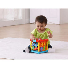 Infant playing with a colorful plastic activity cube toy with blue base and red top
