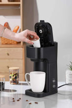 Black matte single-serve coffee maker with hand inserting a cup under the spout