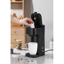 Black matte coffee maker with user placing a coffee pod into the chamber.